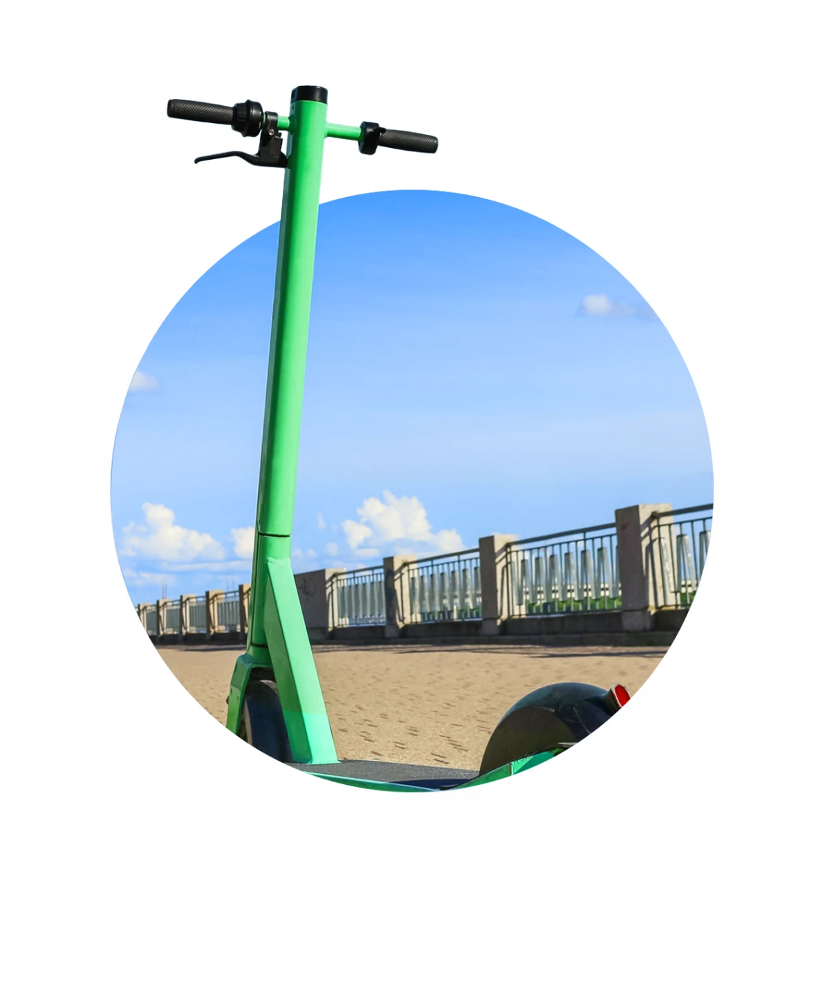A green electric scooter is parked on a sandy path next to a metal railing, with a clear blue sky and clouds in the background, viewed through a circular frame.